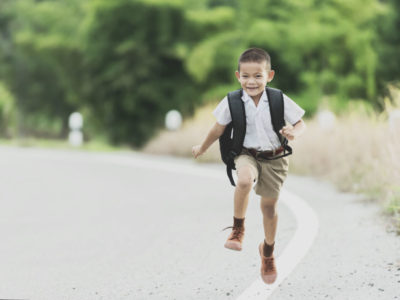 Niño asiático con una mochila corre por una carretera camino a la escuela