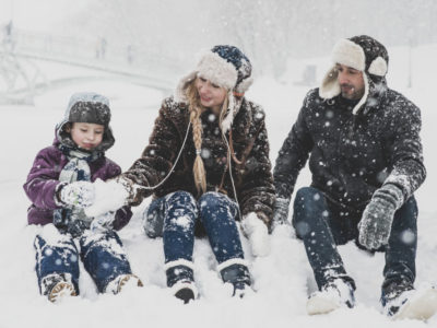 Padre, madre y niña sentados haciendo una bola de nieve