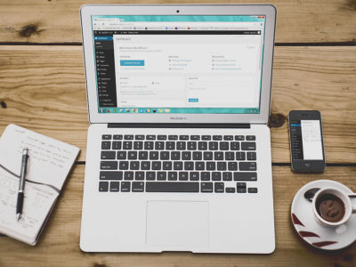 Cuaderno y bolígrafo, ordenador portátil con la interfaz web de Wordpress y taza de café sobre una mesa de madera
