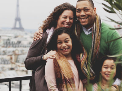 Familia de refugiados (padre, madre y dos hijas) posan sonrientes con la torre Eiffel al fondo.